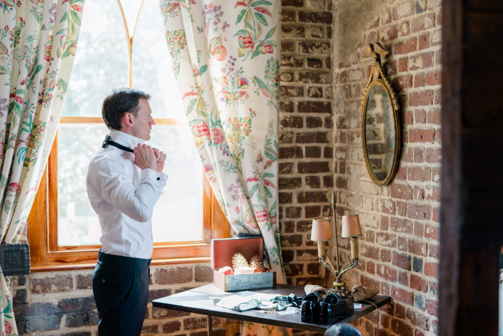 Groom getting ready on the morning of his wedding adjusting his bowtie in the mirror. Charleston destination wedding.