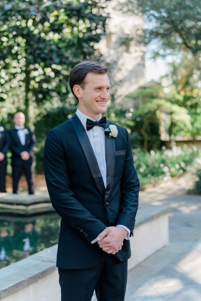 Groom sees bride walking up the aisle at outdoor spring wedding ceremony in Charleston. 