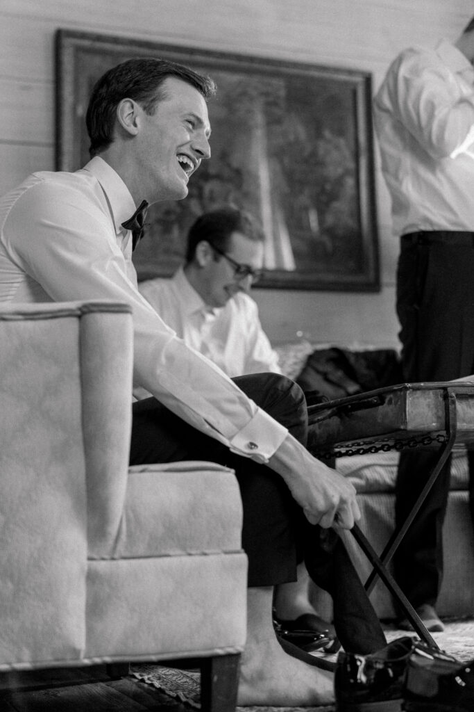 Black and white candid photo of groom putting on his shoes on wedding day.