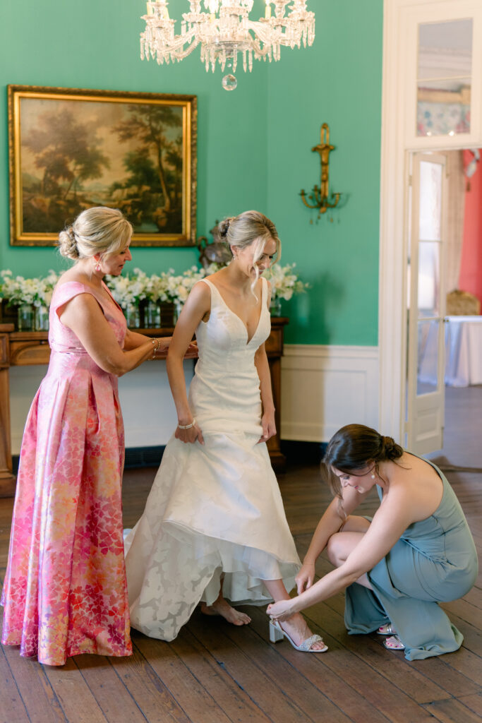 Bride's sister helps her put on her heels on wedding day. William Aiken House spring wedding.