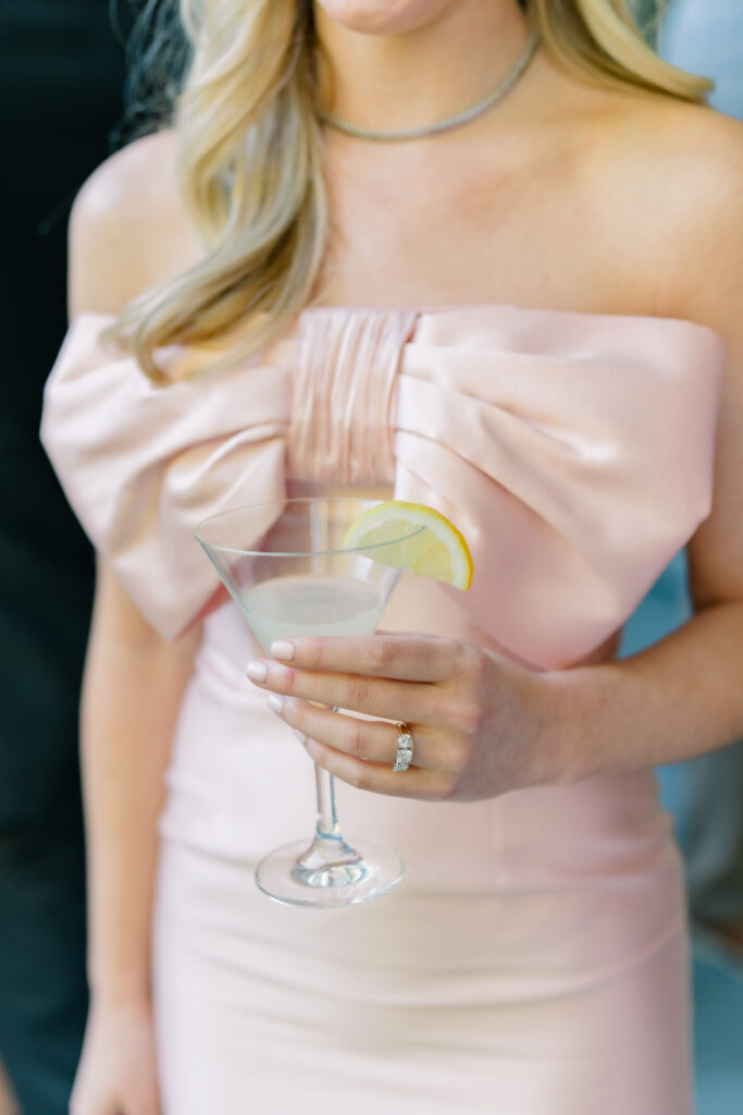 Maid of honor in pink dress with a big bow holding a martini at cocktail hour. 