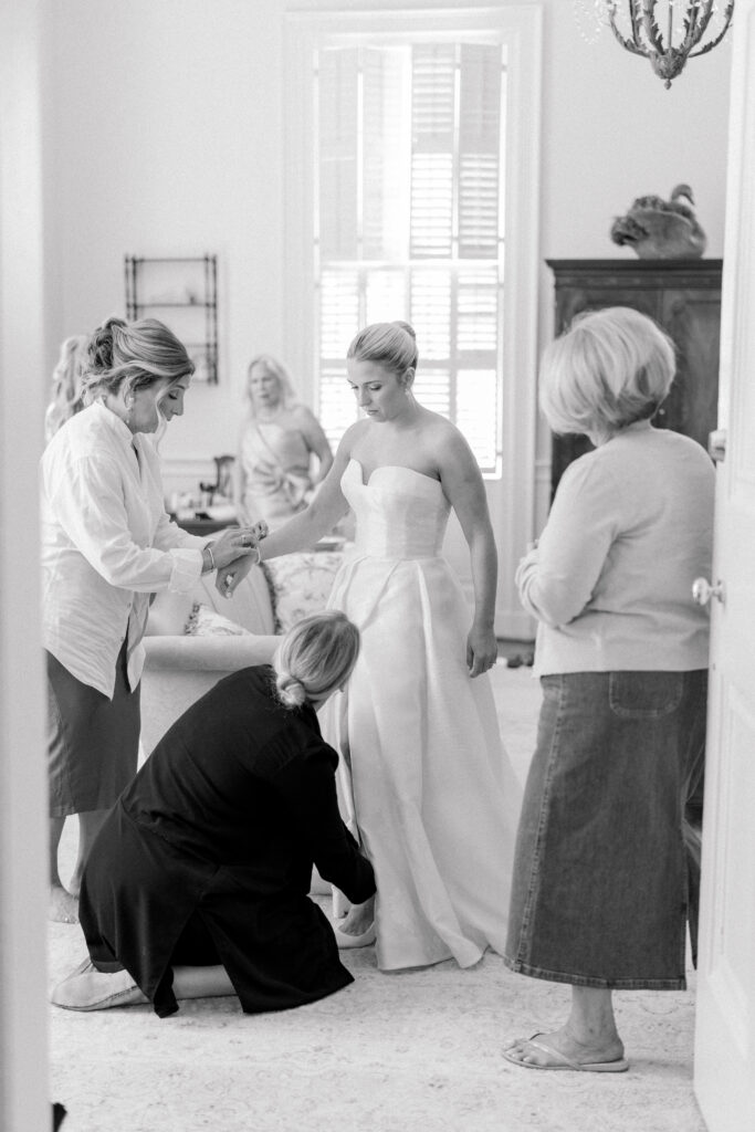 Bride's aunts help her get into heels on wedding day. Black and white candid documentary style wedding photos. 