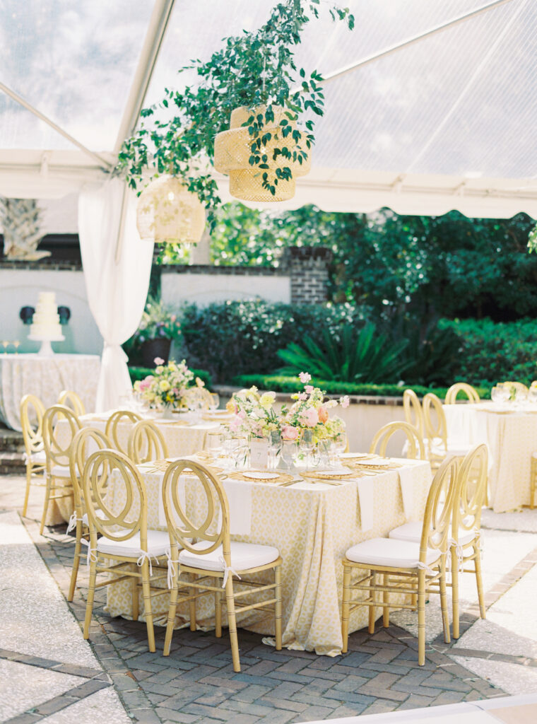 Outdoor pink and yellow wedding reception with hanging greenery and wicker lamps. 