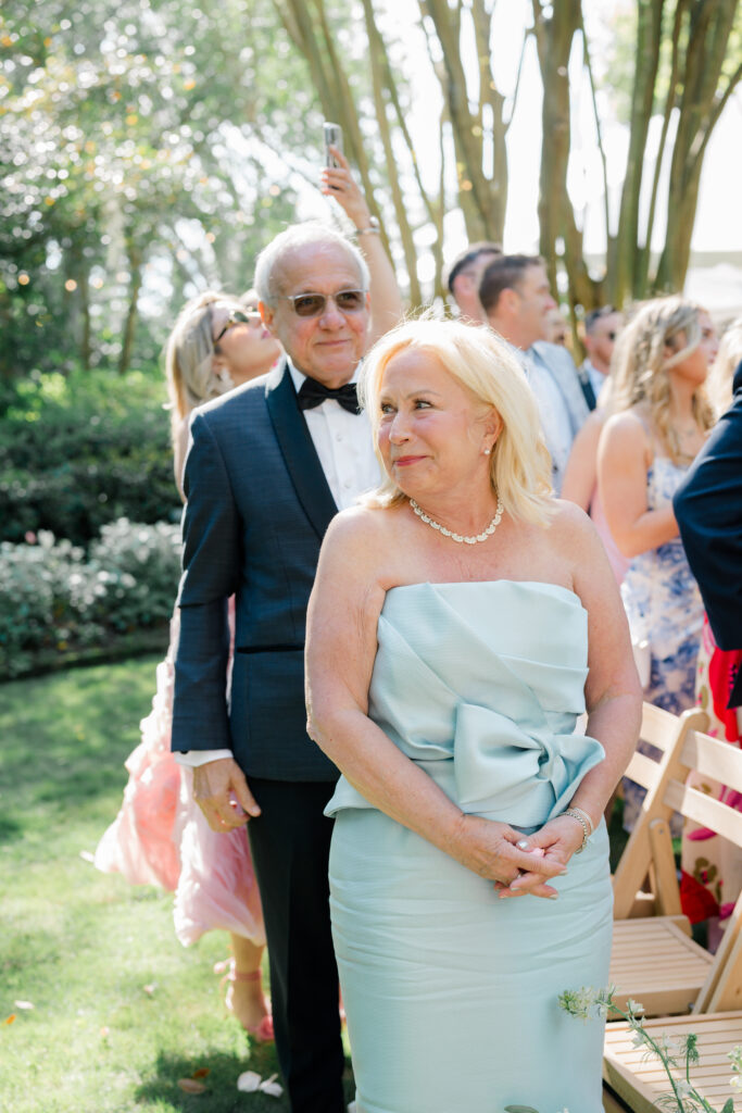 Mother of the groom smiles at son while the bride walks up the aisle. 