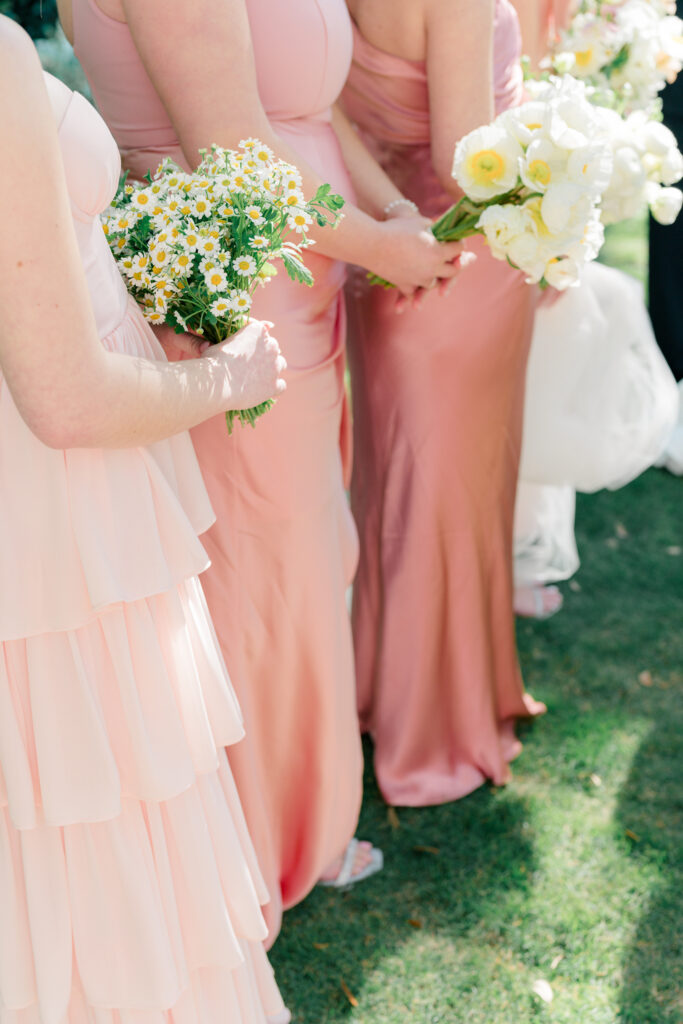 Bridesmaids holding flowers in the sunshine. Outdoor garden wedding ceremony. 