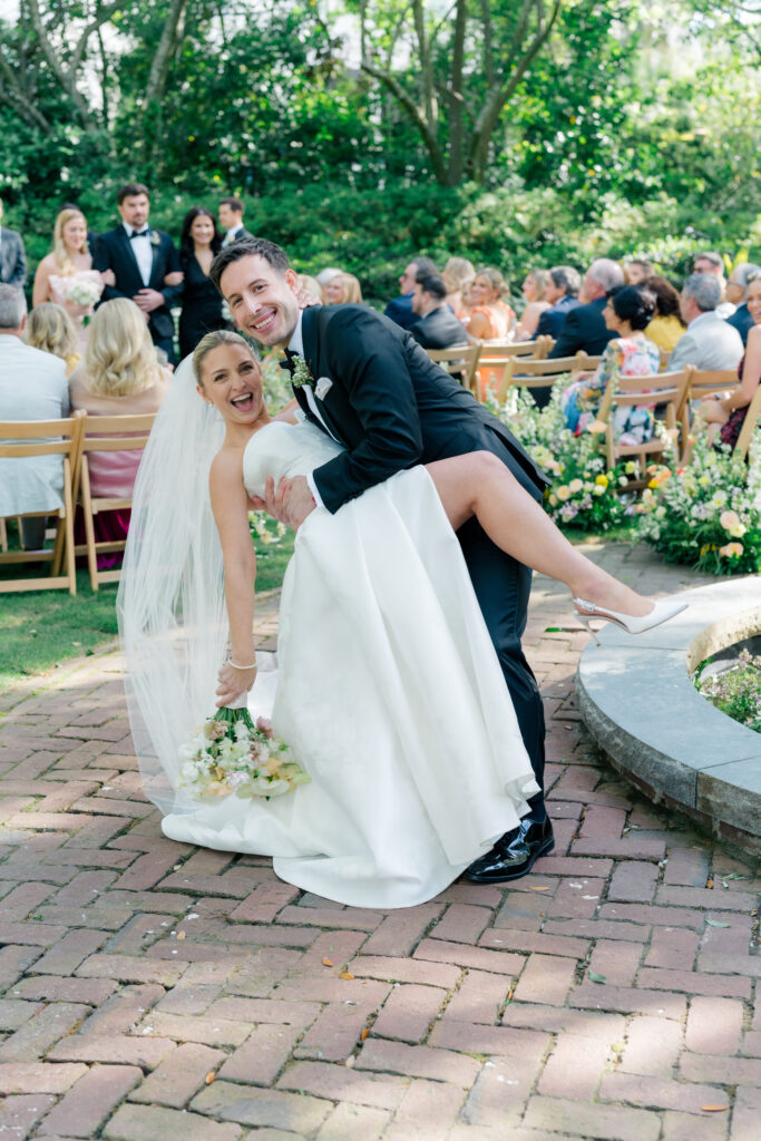 Candid bride and groom wedding ceremony aisle dip kiss. 