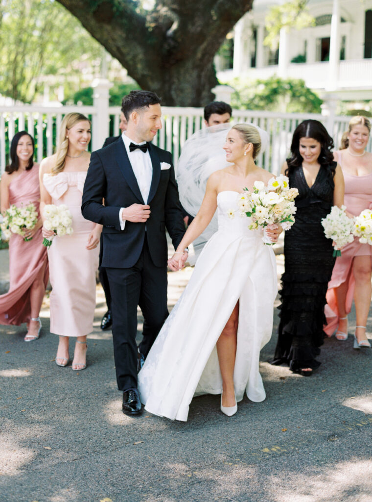 Film photo of bride and groom holding hands and walking with bridal party. 