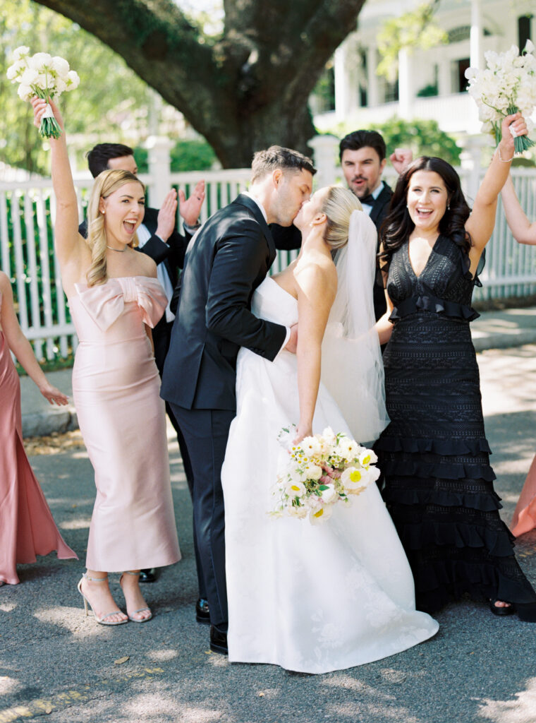 Bride and groom kiss with bridal party celebrating. 