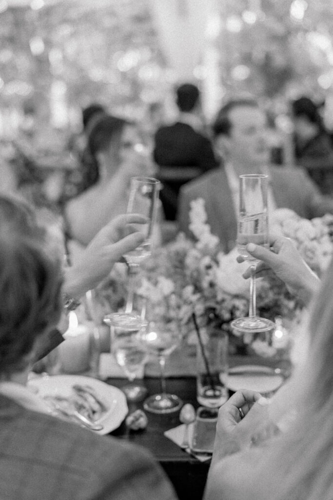 Black and white photo of a champagne toast with bride and groom in the background. 