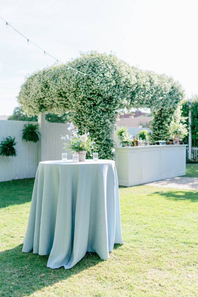 Light blue high top table with bar in the background filled with blooming jasmine. Spring outdoor rehearsal dinner in Beaufort, SC. 