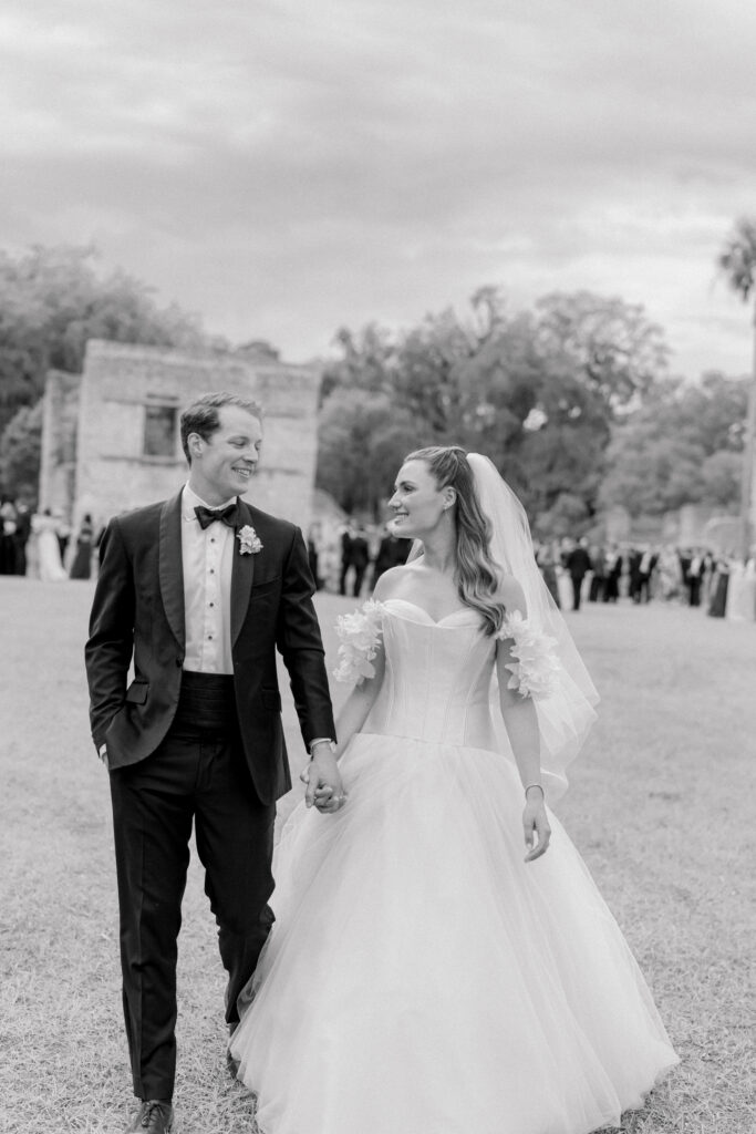 Black and white crooked horizon photo of bride and groom walking away from cocktail hour. 