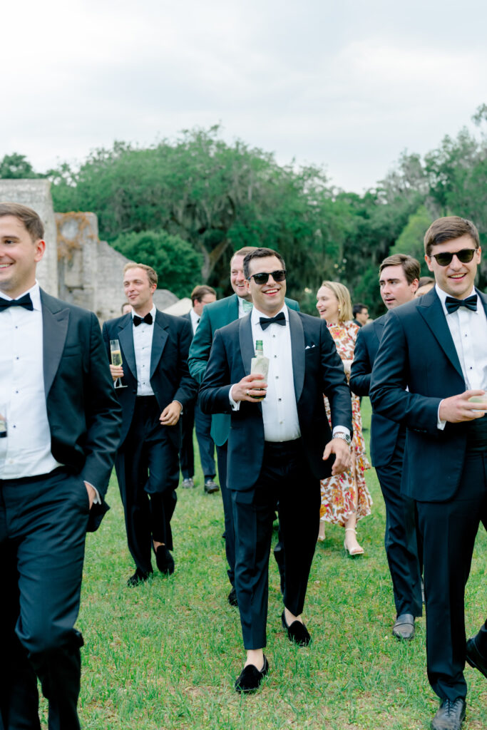 Friends of the groom walking together and laughing at waterfront cocktail hour. 