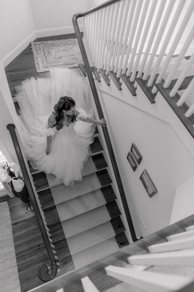 Black and white photo of bride walking down the steps in her house on Spring Island. 