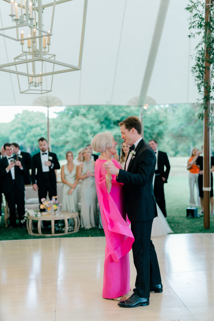 Groom dances with his mom. Bright pink mother of the bride dress. 