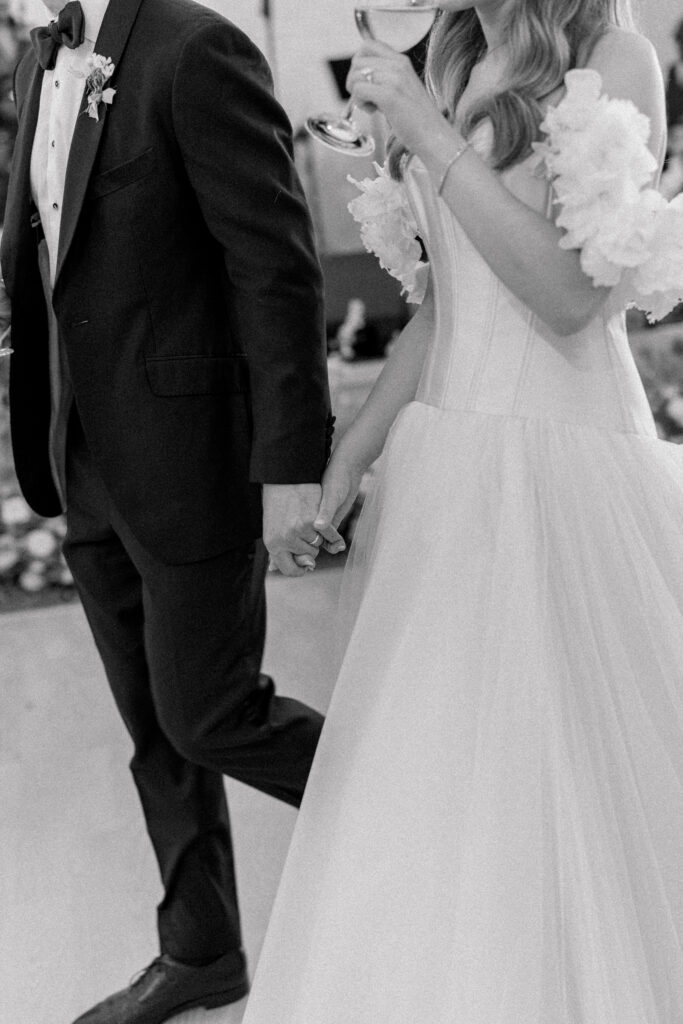 Black and white photo of bride and groom holding hands after father of the bride speech. 