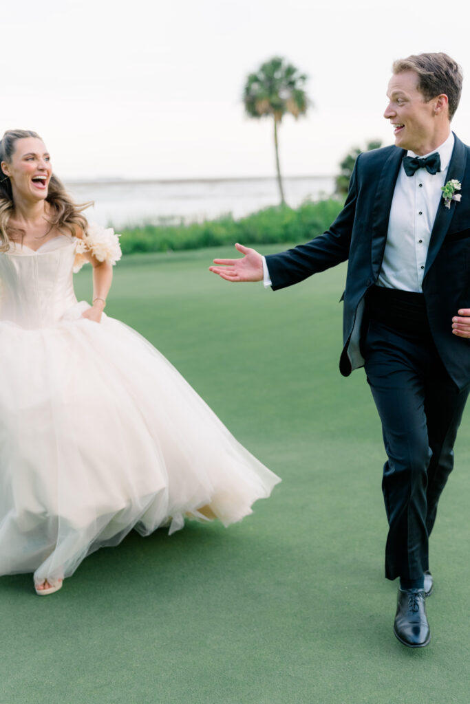 Fun wedding photo of bride and groom running together with water and palm tree in background. 