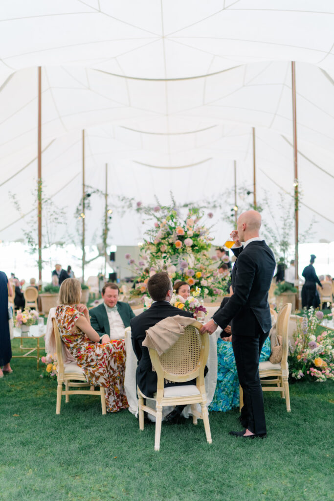 Wedding guests sit down for dinner in grand sperry tent. 