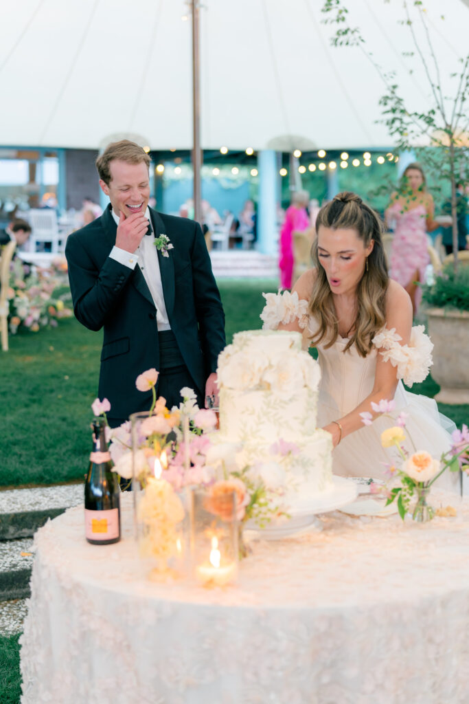 Groom laughing with bride attempting to get a piece out of the cake. 