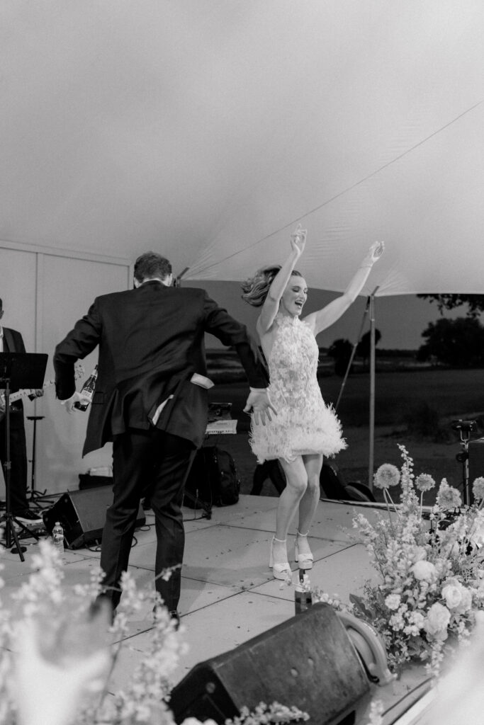 Black and white candid photo of bride and groom on stage dancing. 