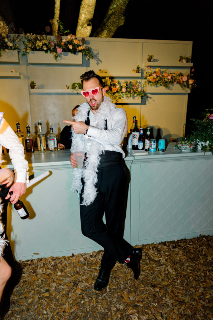 Best man lets loose at wedding reception. White boa and pink heart sunglasses. 