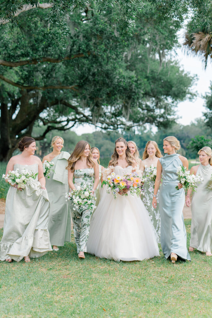 Bride in blush pink dress walking with bridesmaids in mix-match green dresses. Different fabrics and shades of green. 