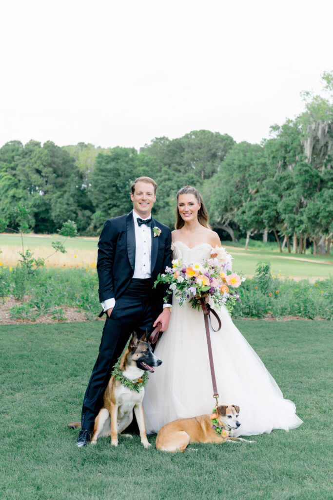 Bride and groom standing with their dogs in green grass.