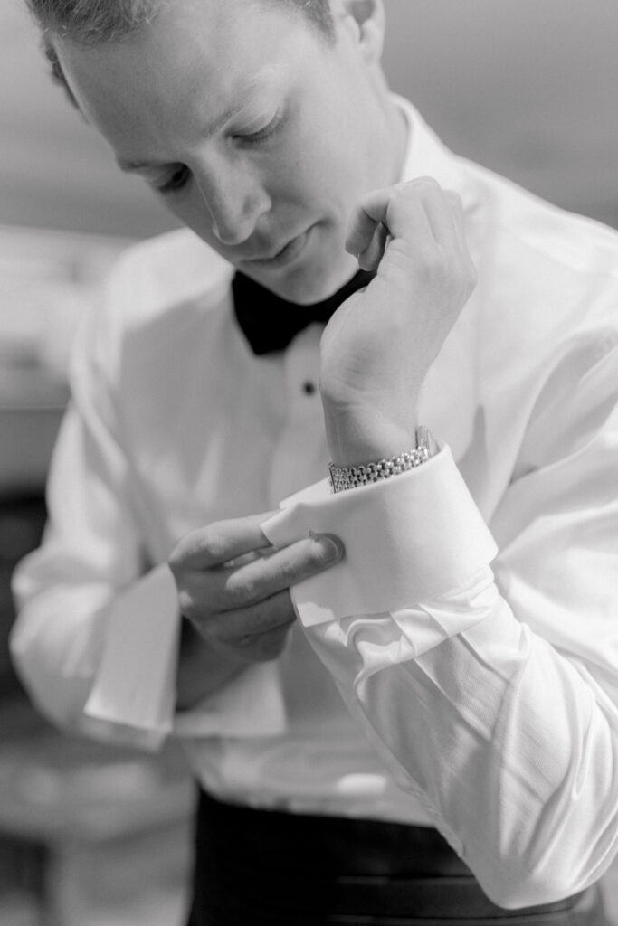 Black and white photo of groom putting on cufflinks. 