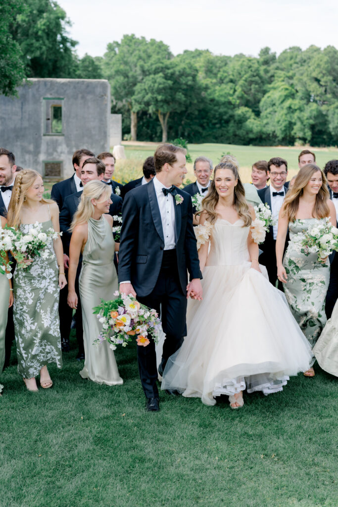 Bride and groom walking with bridal party. Groom holding bride's flowers. 