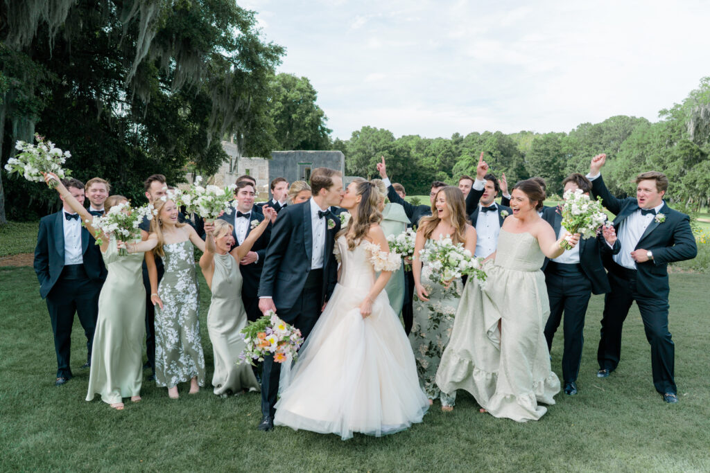 Bride and groom kiss with full bridal party celebrating. 