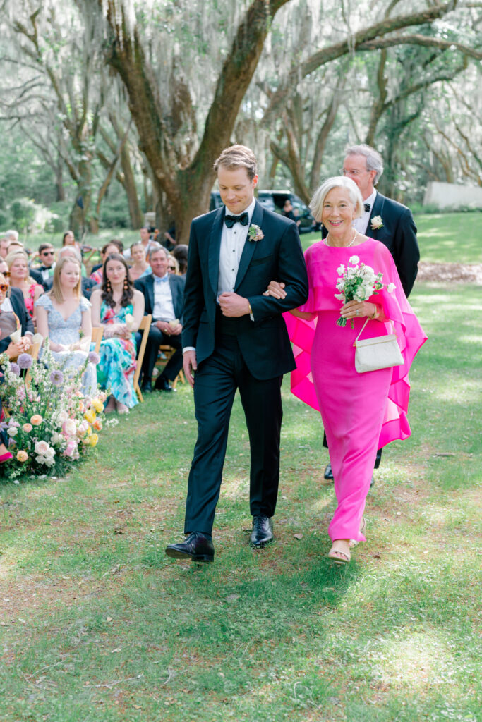 Bright pink mother of the groom dress. Groom escorting his mom at outdoor wedding ceremony. 