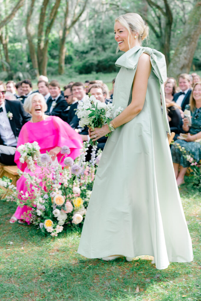 Groom's sister laughs with mother of the groom while walking in at wedding ceremony. 