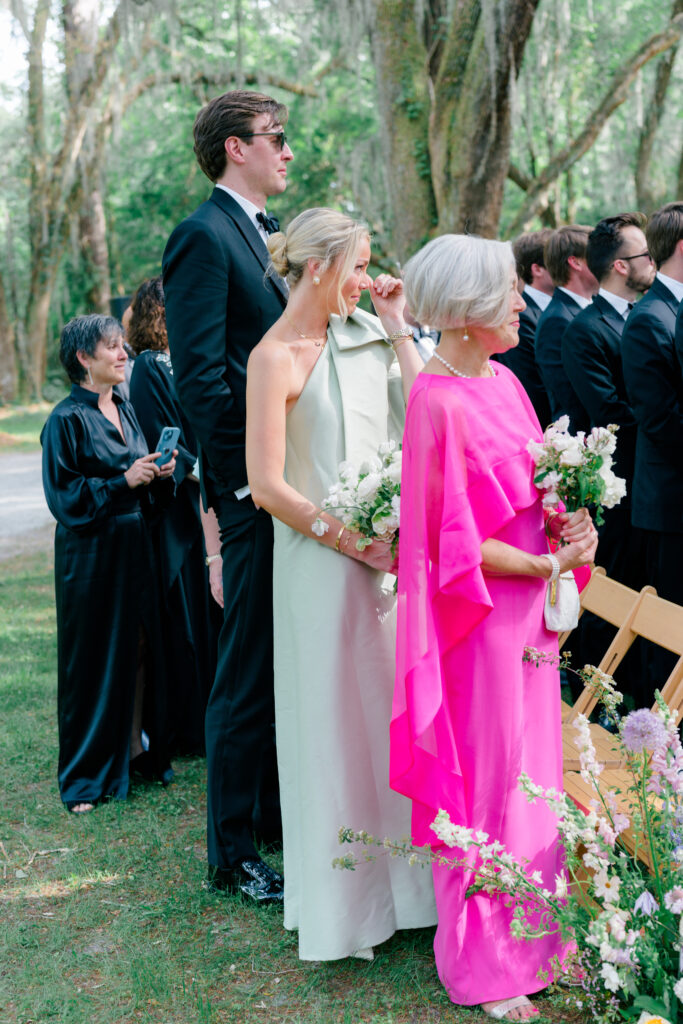 Groom's family sees the bride walking up the aisle. Bright pink mother of the groom dress. 
