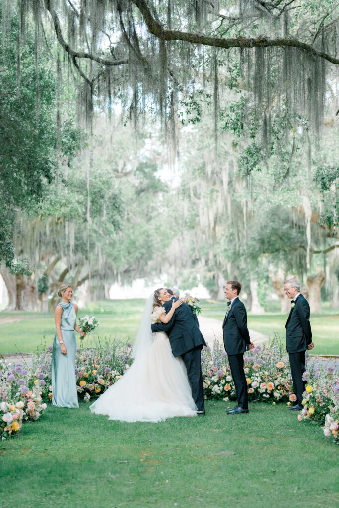 Bride hugs her dad at wedding ceremony under grand spanish moss. 