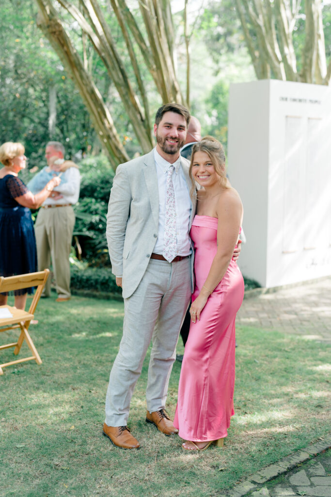 Wedding guest style. Girl in pink dress, guy in light suit and floral tie. Cocktail hour in the garden in downtown Charleston. 