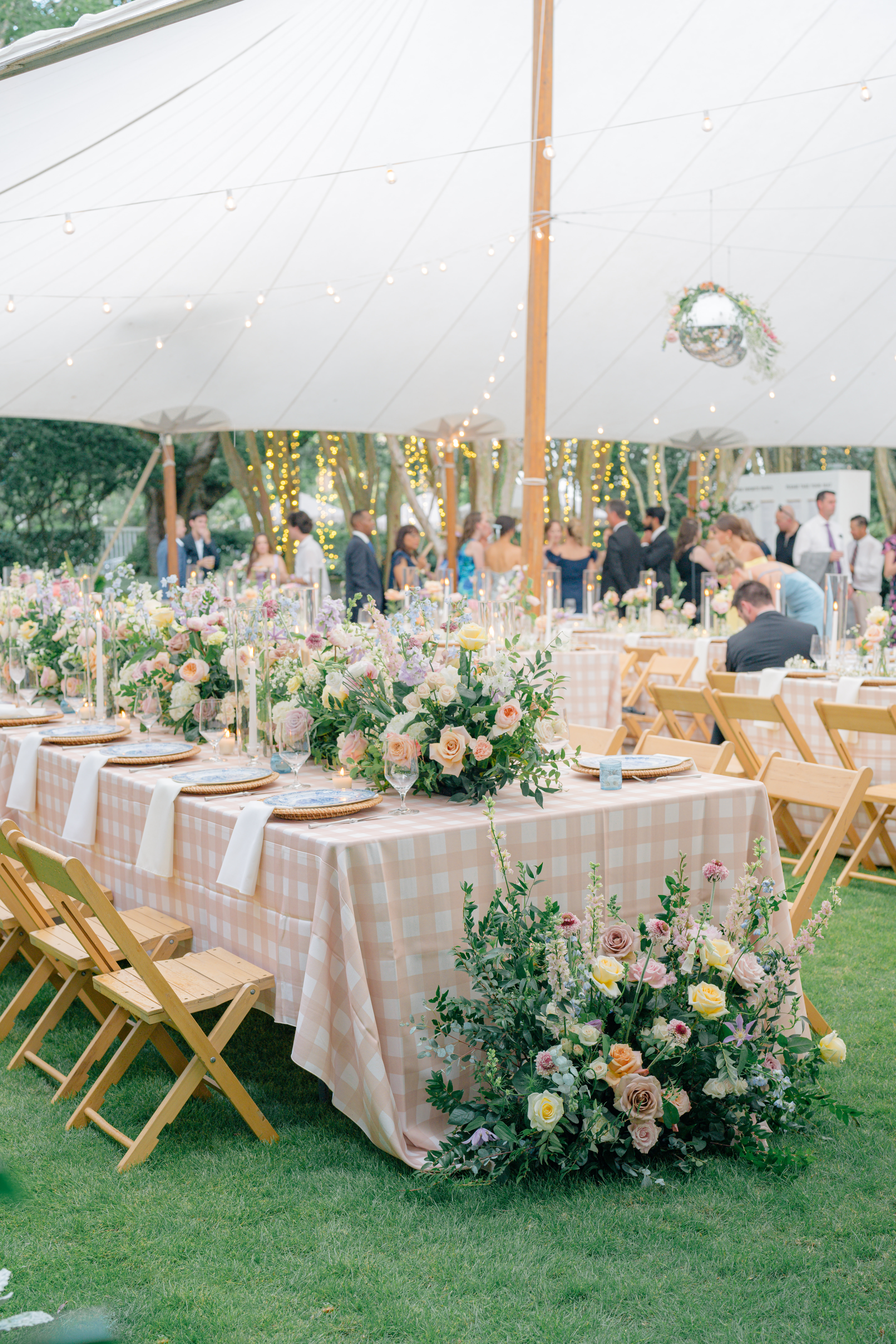 Overall tent shot. Sailcloth tent with hanging disco balls. Grand head table with floral runner. Gingham table linen and blue china plates. 