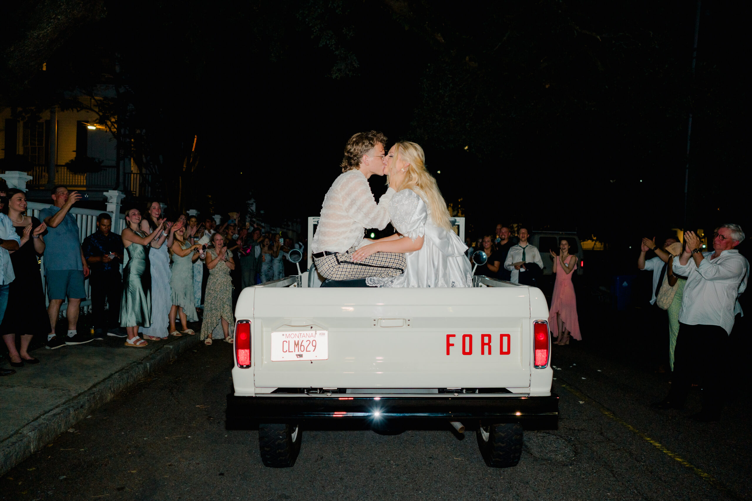 Bride and groom kiss in the back of vintage white bronco getaway car. 