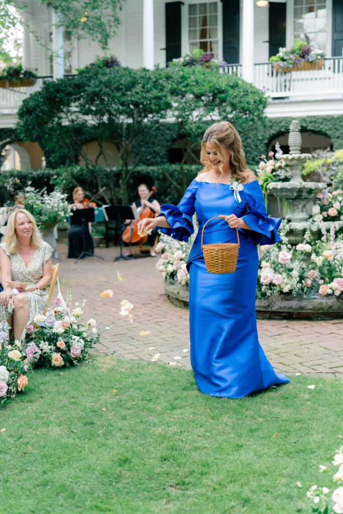 Mother of the bride in bold blue dress acts as flower girl for outdoor wedding ceremony at Thomas Bennett House.