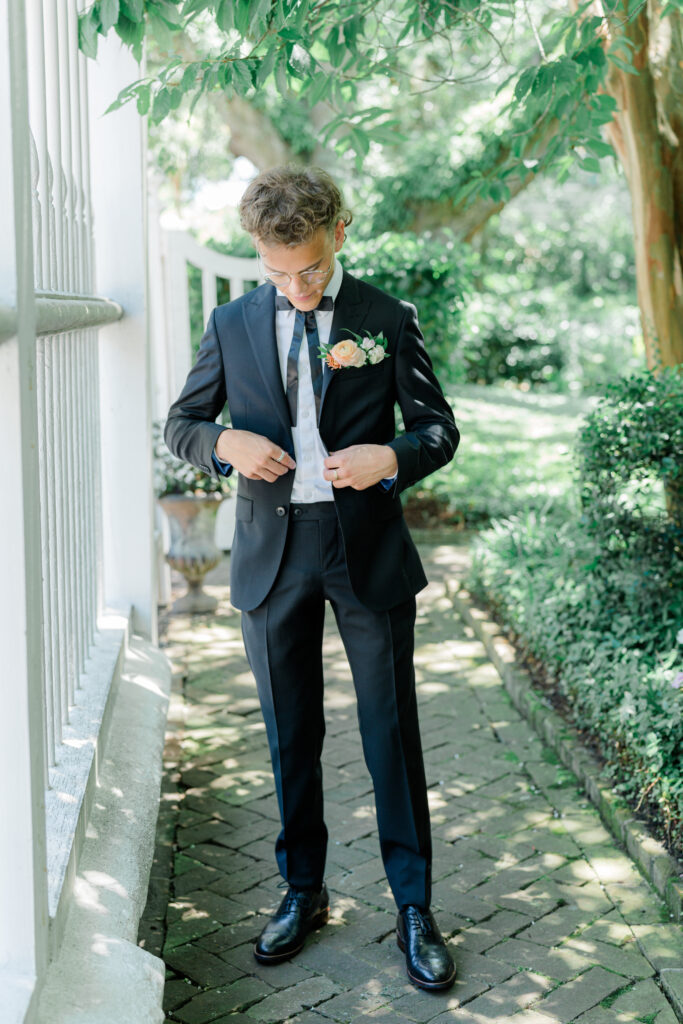 Groom buttoning his tuxedo jacket. 