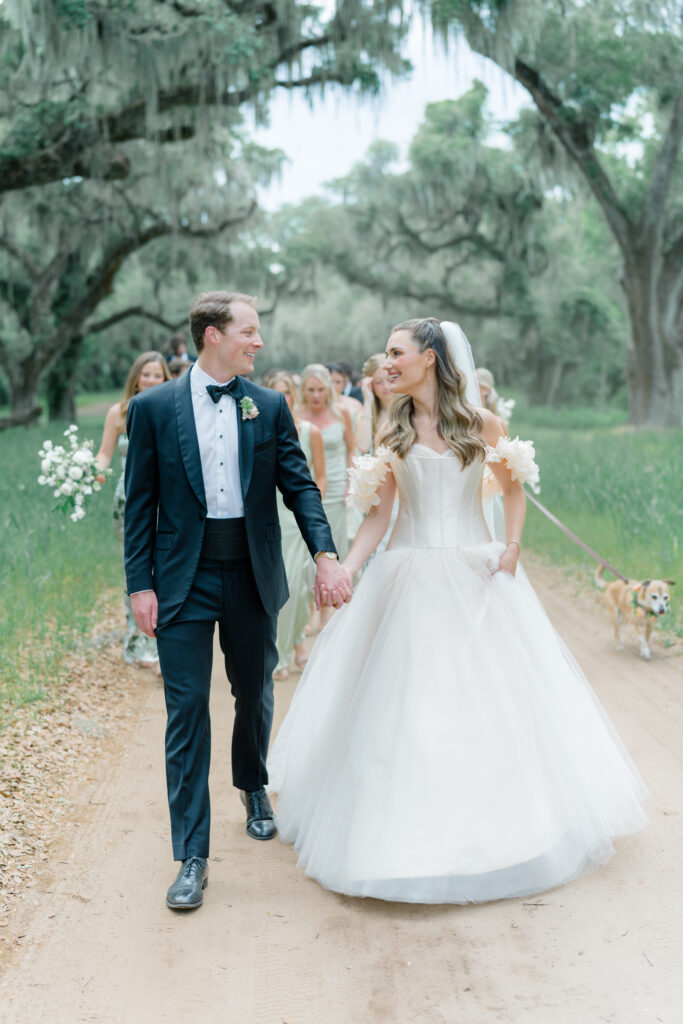 Bride and groom lead wedding guests down dirt road from wedding ceremony to cocktail hour. 