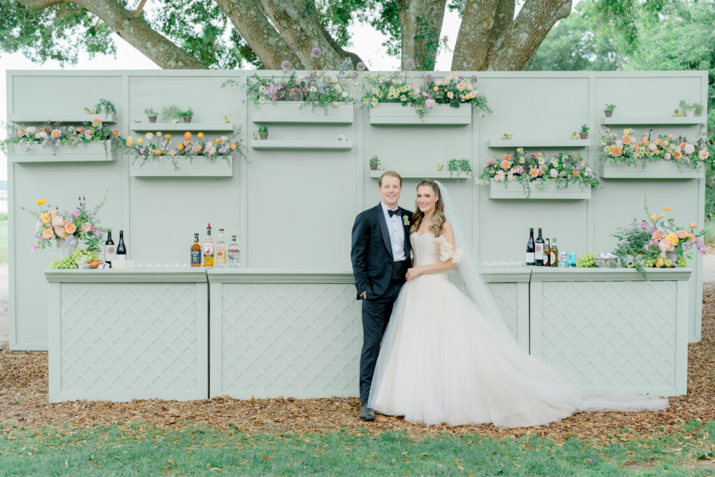 Bride and groom stand in front of grand light green bar. 