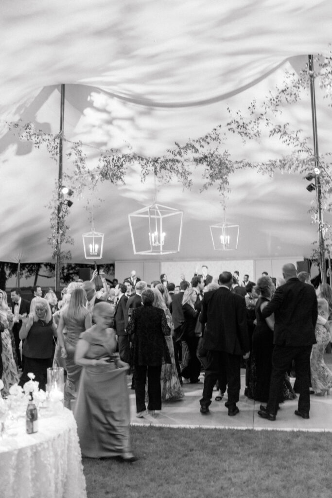 Black and white photo of reception tent with wedding guest walking. 