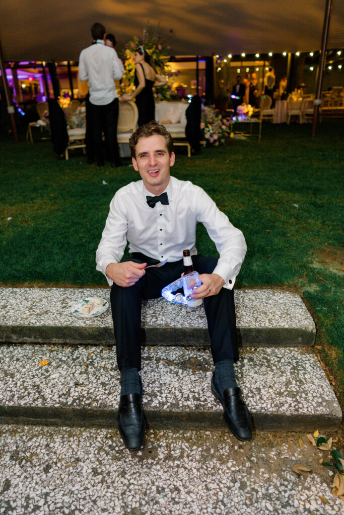 Wedding guest sits down on step to enjoy a slice of cake. 