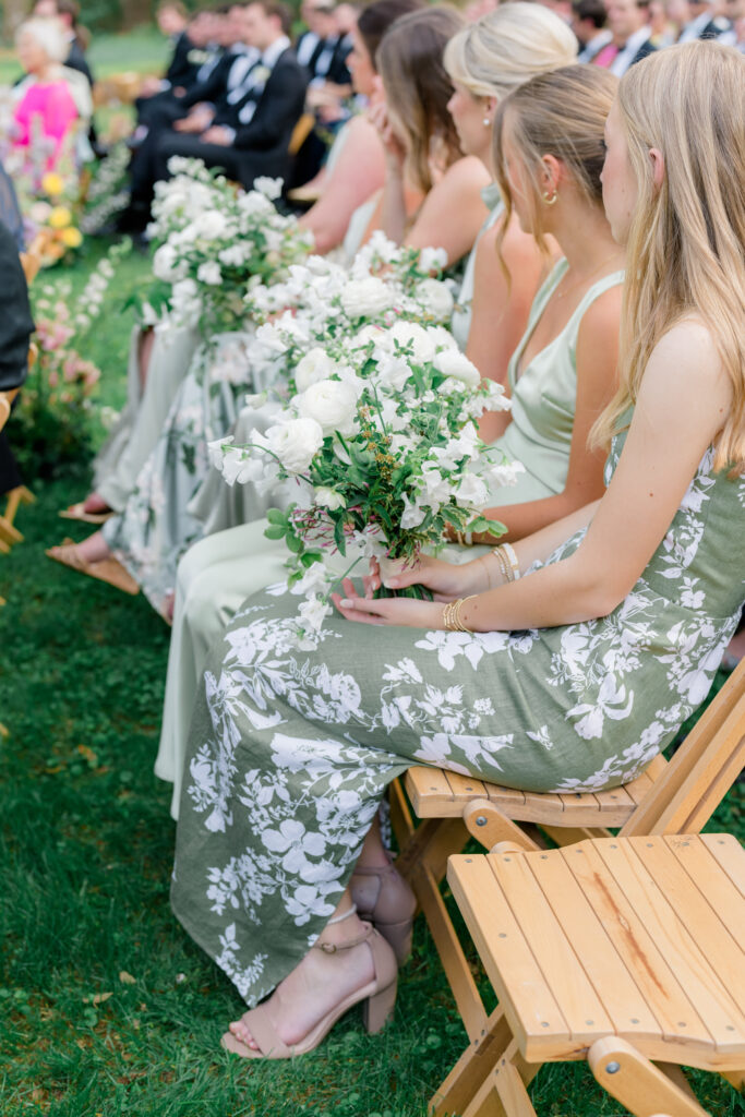 Mix-matched green bridesmaids dresses. Bridesmaids sitting in second row of ceremony. 