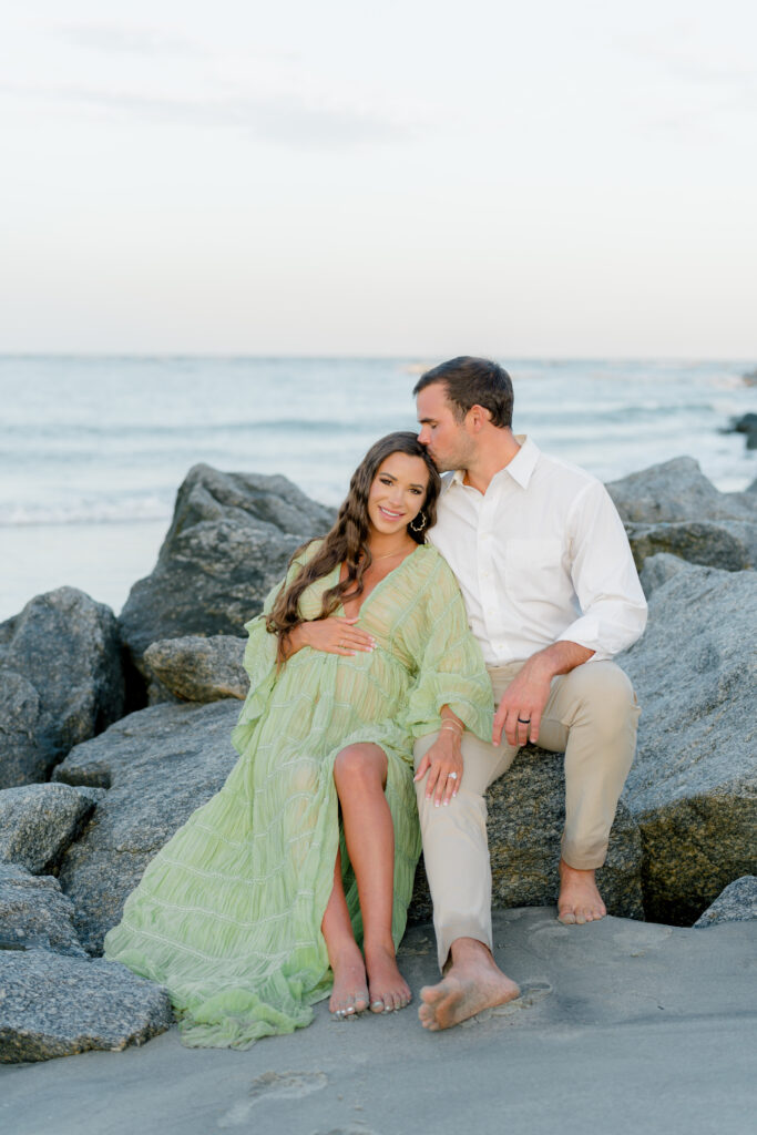 Couple sitting on the rocks on the beach. Charleston spring maternity session. 