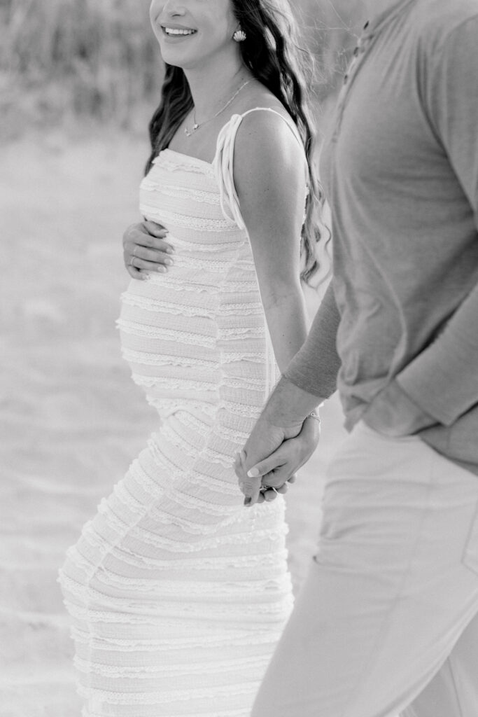 Black and white photo of girl holding pregnant belly and holding hands white walking by. 