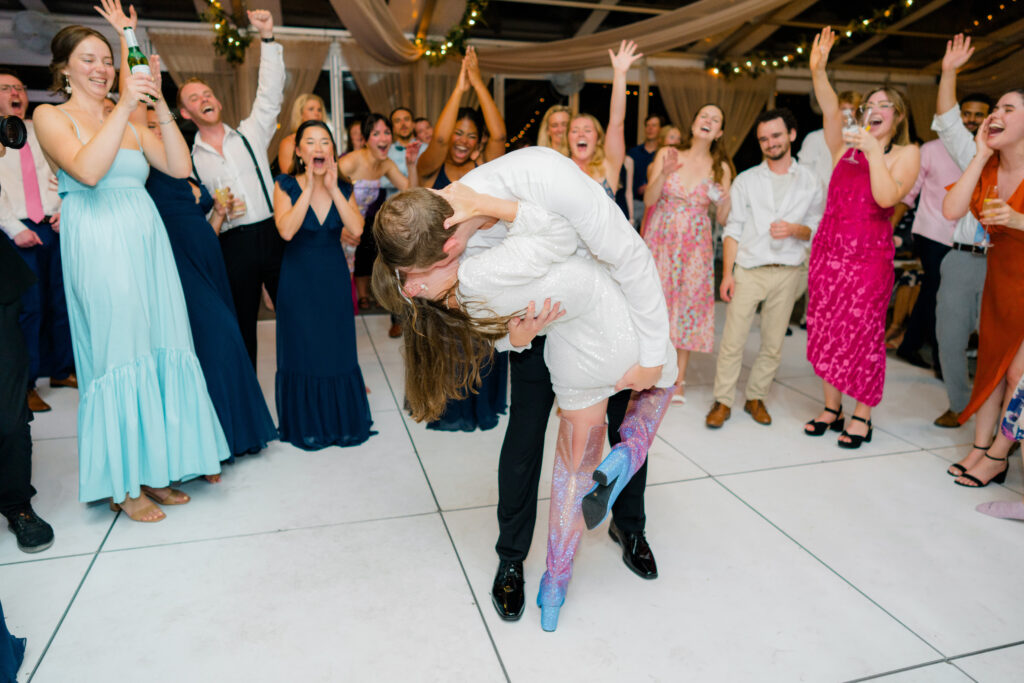 Bride and groom dip kiss with crowd celebrating in the background. 