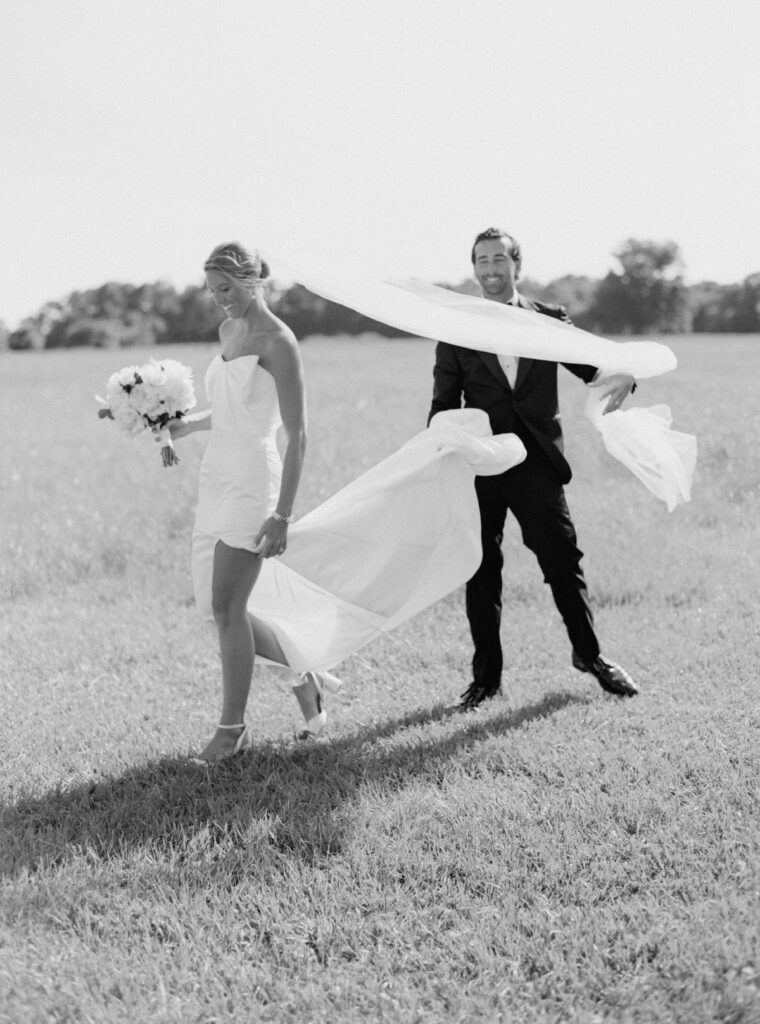 Groom helps the bride with her dress and veil. Candid black and white wedding photos. 