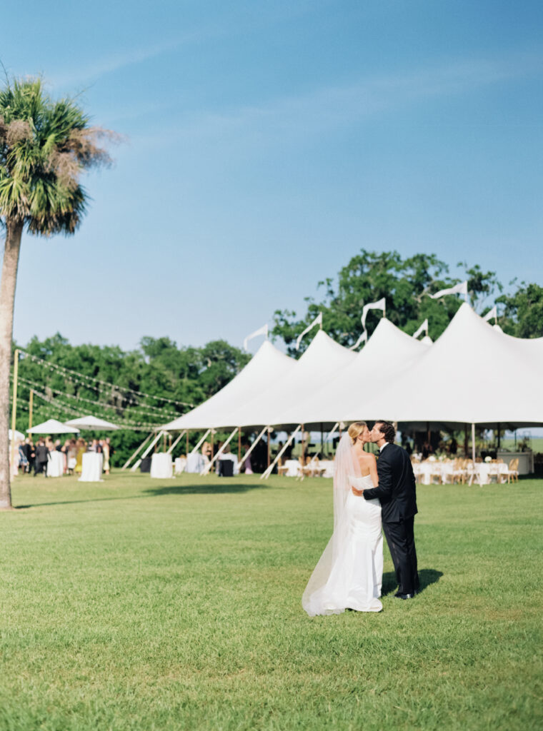 Bride and groom kiss with sailcloth tent in background.