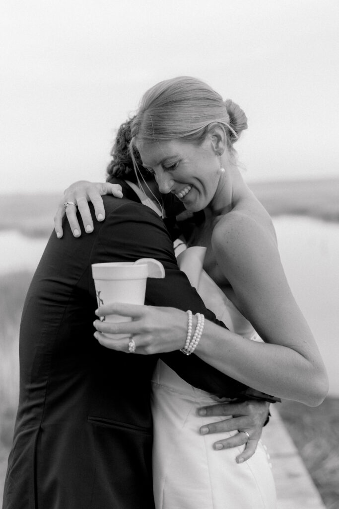 Black and white photo of bride hugging groom while holding custom styrofoam cup. 