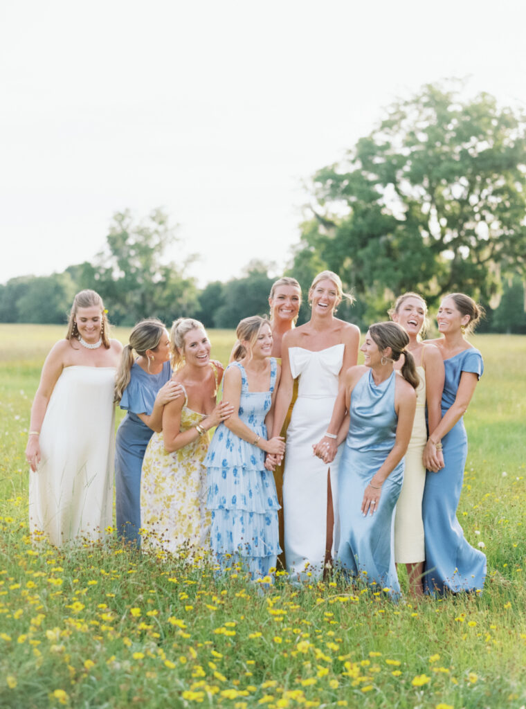 Bride and bridesmaids laugh in the field covered with wildflowers. 